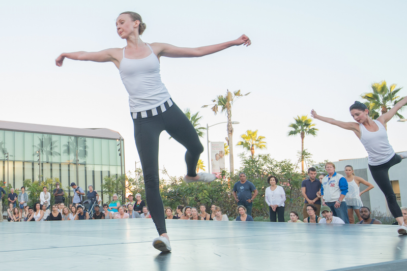 Kaitlyn Gilliland and Ramona Kelly dance on a stage outdoors before a crowd of people in LA